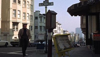 Movie still from “Bullitt” (1968), directed by Peter Yates – A man walking down a street next to a newspaper stand; Wide shot, Low angle