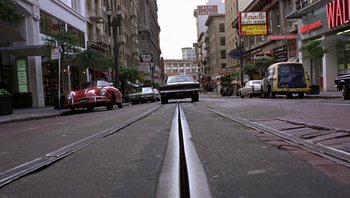 Movie still from “Bullitt” (1968), directed by Peter Yates – A car driving down a street next to some buildings; Extreme Wide shot, High angle
