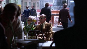 Movie still from “Bullitt” (1968), directed by Peter Yates – An older man and woman sitting at an outdoor cafe; Wide shot, Over the shoulder angle