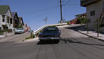 Movie still from “Bullitt” (1968), directed by Peter Yates – A car driving down a street next to power lines; Extreme Wide shot, High angle