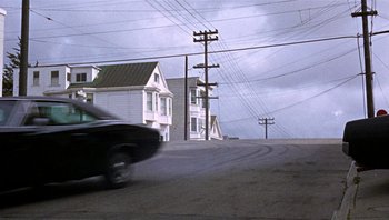 Movie still from “Bullitt” (1968), directed by Peter Yates – A car driving down a street next to power lines; Wide shot, High angle