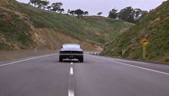 Movie still from “Bullitt” (1968), directed by Peter Yates – A car driving down a road near some hills; Wide shot, High angle