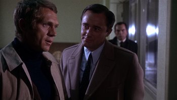 Movie still from “Bullitt” (1968), directed by Peter Yates – A man in a suit and tie standing next to another man in a suit and tie; Medium shot, Over the shoulder angle