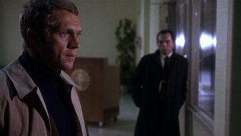 Movie still from “Bullitt” (1968), directed by Peter Yates – A man in a suit and tie standing next to another man in a suit and tie; Medium shot, Over the shoulder angle