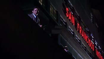 Movie still from “Bullitt” (1968), directed by Peter Yates – A man in a suit standing on a balcony at night in front of a building; Wide shot, Low angle