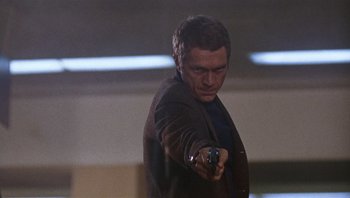 Movie still from “Bullitt” (1968), directed by Peter Yates – A man holding a gun while standing in front of a wall; Medium shot, Low angle