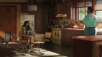 Movie still from “Bumblebee” (2018), directed by Travis Knight – A woman sitting at a table in a kitchen; Wide shot, High angle