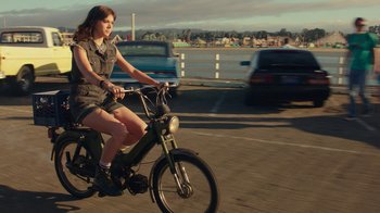 Movie still from “Bumblebee” (2018), directed by Travis Knight – A woman is riding a bike down the street; Wide shot, High angle