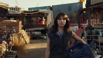 Movie still from “Bumblebee” (2018), directed by Travis Knight – A woman standing in an open area holding a box; Medium shot, Over the shoulder angle