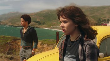 Movie still from “Bumblebee” (2018), directed by Travis Knight – Two young people standing next to each other near a body of water; Medium shot, Over the shoulder angle