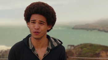 Movie still from “Bumblebee” (2018), directed by Travis Knight – A young man with an afro stands in front of the ocean; Close Up shot, Over the shoulder angle