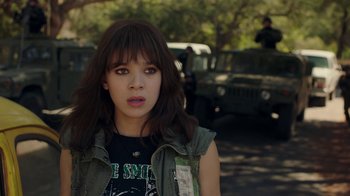 Movie still from “Bumblebee” (2018), directed by Travis Knight – A young woman in a green vest is standing in a parking lot; Close Up shot, Over the shoulder angle