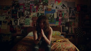 Movie still from “Bumblebee” (2018), directed by Travis Knight – A woman sitting on top of a bed in front of a bunch of posters; Medium shot, High angle