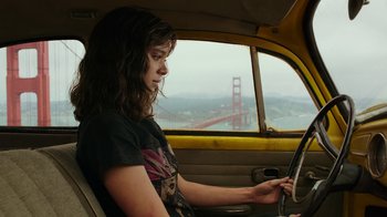 Movie still from “Bumblebee” (2018), directed by Travis Knight – A woman sitting in the driver's seat of a yellow car; Medium shot, Over the shoulder angle