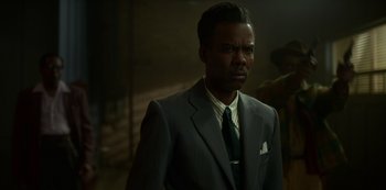Movie still from “Fargo” (2014), created by Noah Hawley – A man in a suit and tie standing in a dark room; Medium shot, Over the shoulder angle
