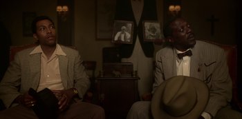Movie still from “Fargo” (2014), created by Noah Hawley – Two men in suits sitting in front of a picture of an old man; Medium shot, Over the shoulder angle