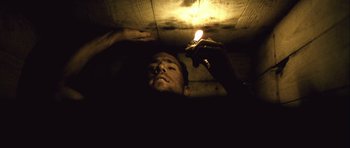 Movie still from “Buried” (2010), directed by Rodrigo Cortés – A man is holding a candle in a dark room; Medium shot, Overhead angle