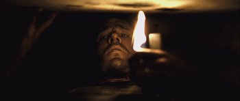 Movie still from “Buried” (2010), directed by Rodrigo Cortés – A man looking at a candle in a dark room; Close Up shot, Overhead angle