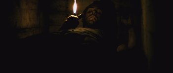 Movie still from “Buried” (2010), directed by Rodrigo Cortés – A man lighting a candle in a dark room; Medium shot, Overhead angle