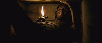 Movie still from “Buried” (2010), directed by Rodrigo Cortés – A man is holding a lit candle in a dark room; Medium shot, Overhead angle