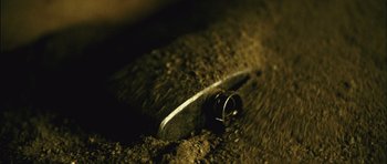 Movie still from “Buried” (2010), directed by Rodrigo Cortés – A knife stuck in the ground next to a ring; Extreme Close Up shot, Overhead angle