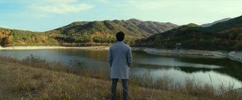 A man standing in a field looking at a lake