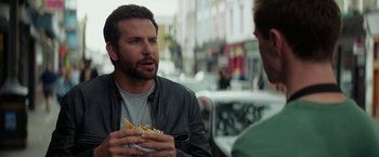 Movie still from “Burnt” (2015), directed by John Wells – A man holding a hot dog in front of another man; Close Up shot, Over the shoulder angle