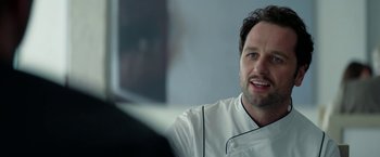 A man in a chef's outfit sitting in front of a computer screen