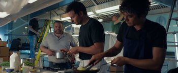 Movie still from “Burnt” (2015), directed by John Wells – A group of people standing around a kitchen preparing food; Medium shot, Over the shoulder angle