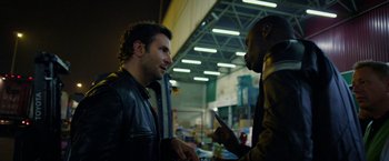 Movie still from “Burnt” (2015), directed by John Wells – Two men talking to each other in an indoor area; Medium shot, Over the shoulder angle