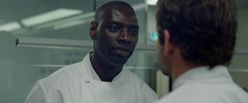 Movie still from “Burnt” (2015), directed by John Wells – A man wearing a white chef's uniform talking to another man in front of a mirror; Close Up shot, Over the shoulder angle