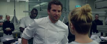 Movie still from “Burnt” (2015), directed by John Wells – A man and a woman in white chef's uniforms; Medium shot, Over the shoulder angle