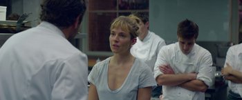 Movie still from “Burnt” (2015), directed by John Wells – A woman in a white shirt is standing in front of a group of people; Close Up shot, Over the shoulder angle