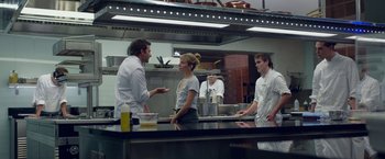 Movie still from “Burnt” (2015), directed by John Wells – A group of people standing in a restaurant kitchen; Medium shot, Over the shoulder angle
