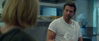 Movie still from “Burnt” (2015), directed by John Wells – A man sitting in front of a woman in front of a counter; Medium shot, Over the shoulder angle