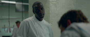 Movie still from “Burnt” (2015), directed by John Wells – A man in a chef's outfit looking at another man; Close Up shot, Over the shoulder angle