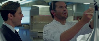 Movie still from “Burnt” (2015), directed by John Wells – A man wearing a white chef's outfit in a kitchen; Close Up shot, Low angle