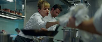 Movie still from “Burnt” (2015), directed by John Wells – A woman and a man working in a restaurant kitchen; Medium shot, Low angle