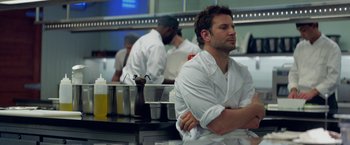 Movie still from “Burnt” (2015), directed by John Wells – A group of people in a kitchen preparing food; Medium shot, Over the shoulder angle