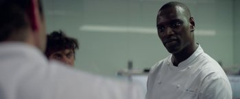 Movie still from “Burnt” (2015), directed by John Wells – A man wearing a white chef's outfit standing in front of another man; Close Up shot, Over the shoulder angle