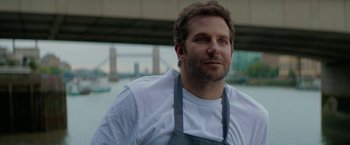 Movie still from “Burnt” (2015), directed by John Wells – A person wearing an apron; Close Up shot, Over the shoulder angle