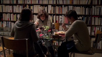 Movie still from “Caché” (2005), directed by Michael Haneke – A group of people sitting at a table in front of a bookshelf; Medium shot, Over the shoulder angle