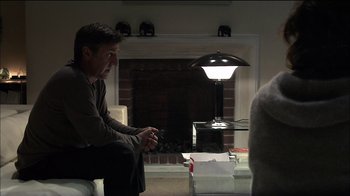 Movie still from “Caché” (2005), directed by Michael Haneke – A man sitting in front of a fireplace holding a nintendo wii controller; Medium shot, Over the shoulder angle