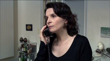 Movie still from “Caché” (2005), directed by Michael Haneke – A woman talking on a phone while wearing a black shirt; Close Up shot, Over the shoulder angle