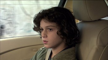 Movie still from “Caché” (2005), directed by Michael Haneke – A young boy sitting in the back seat of a car; Close Up shot, Over the shoulder angle