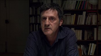 Movie still from “Caché” (2005), directed by Michael Haneke – A person sitting in front of a book shelf; Close Up shot, Over the shoulder angle