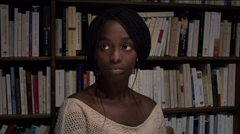 Movie still from “Caché” (2005), directed by Michael Haneke – A young woman in front of bookshelves in a library; Close Up shot, Over the shoulder angle