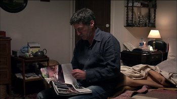 Movie still from “Caché” (2005), directed by Michael Haneke – A man sitting on a bed looking at a photo album; Medium shot, High angle