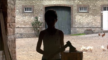 Movie still from “Caché” (2005), directed by Michael Haneke – A young boy holding a axe in front of a brick building; Wide shot, Low angle