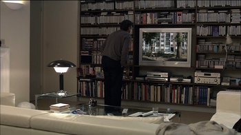 Movie still from “Caché” (2005), directed by Michael Haneke – A man standing in front of a television in a living room; Wide shot, High angle